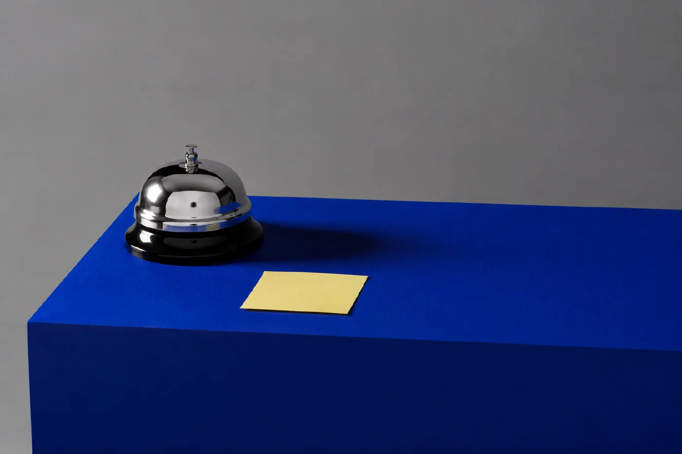 A chrome desk bell and a blank sticky note on a blue pedestal